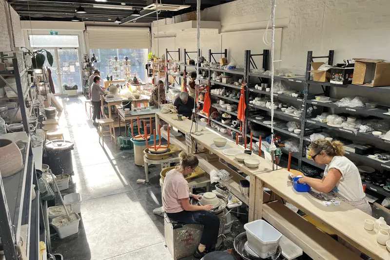 Potters at the wheels and benches in the long Phoenix Pottery studio