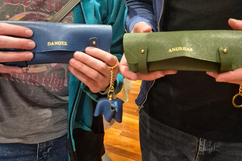 Two people holding up the leather pencil cases they made in a class
